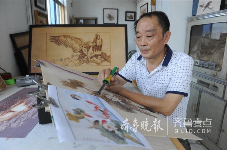 里墙上挂满了大大小小的烙画作品,刘永俊坐在桌前手拿烙铁认真作画